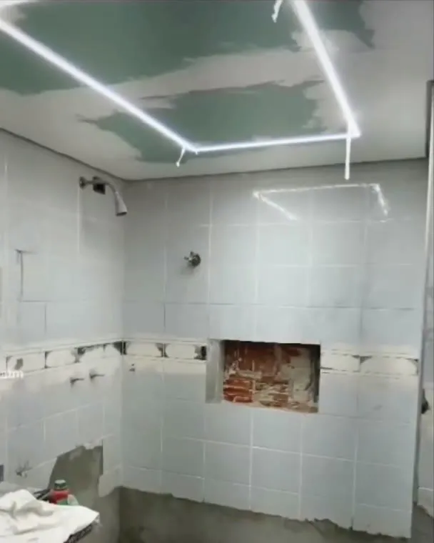Banheiro antes da transformação, com revestimento antigo e teto com iluminação.